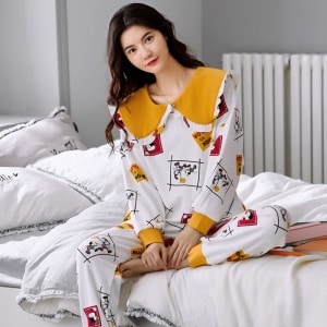 Pijama de manga larga de algodón de alta calidad para mujer, con puños, llevado por una mujer sentada en la cama de una casa