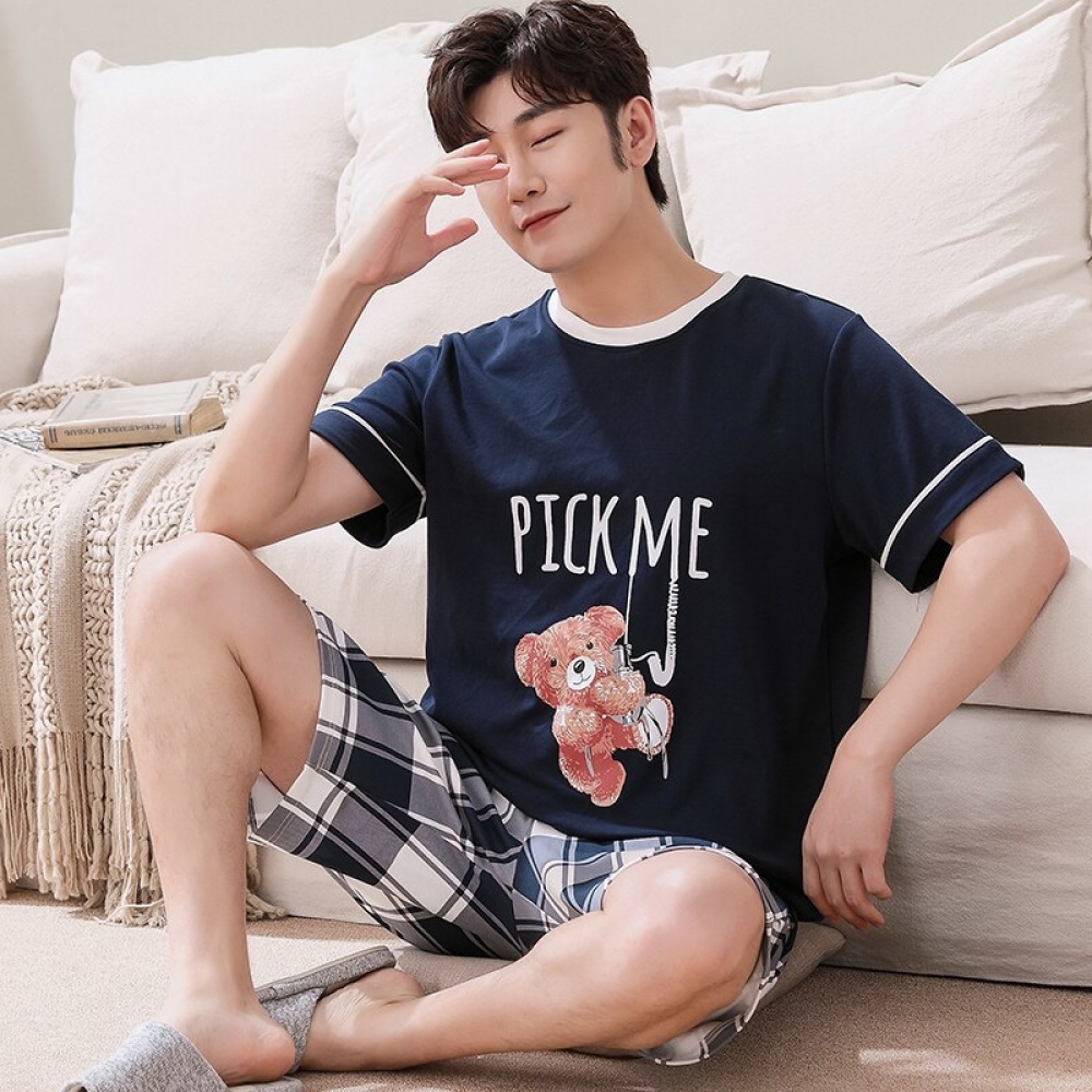 Pijama de verano con camiseta azul y estampado de osos y pantalón corto a cuadros que lleva un hombre sentado en la alfombra de una casa