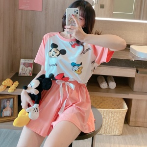 Pijama de verano rosa con estampado de Mickey y Donald que lleva una mujer sentada en una silla tomando un phoo en una casa