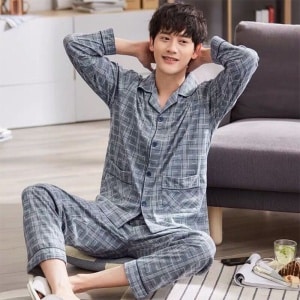 Pijama de hombre a rayas de algodón gris llevado por un hombre sentado en una alfombra delante de un sofá en una casa