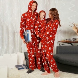 Pijama navideño con capucha para toda la familia, llevado por una familia delante del sofá de una casa