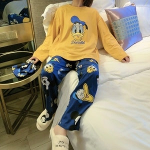 Bonito pijama de mujer Donald de Disney en amarillo mostaza y azul que lleva una mujer sentada en la cama de una casa