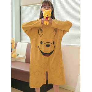 Pijama holgado de mujer amarillo mostaza de Winnie the Pooh que lleva una mujer delante del sofá de una casa