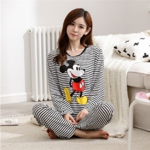 Pijama femenino a rayas de Mickey llevado por una mujer sentada delante de una cama en una casa