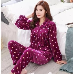 Elegante pijama de invierno morado con pequeños lunares de colores en blanco que lleva una mujer sentada en una alfombra delante de una cama en una casa