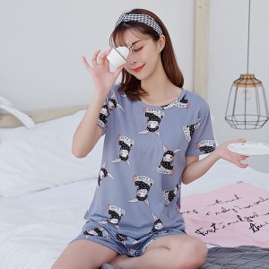 Pijama de verano con camiseta gris y pantalón corto para mujer con estampado de conejos que lleva una mujer sentada en una cama en una casa