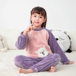 Conjunto de pijama infantil de forro polar morado que lleva una niña sentada en la cama de una casa