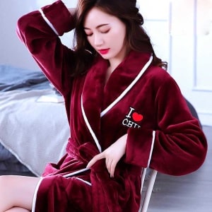 Pijama femenino de forro polar rojo coral de muy alta calidad llevado por una mujer sentada en una silla en una casa