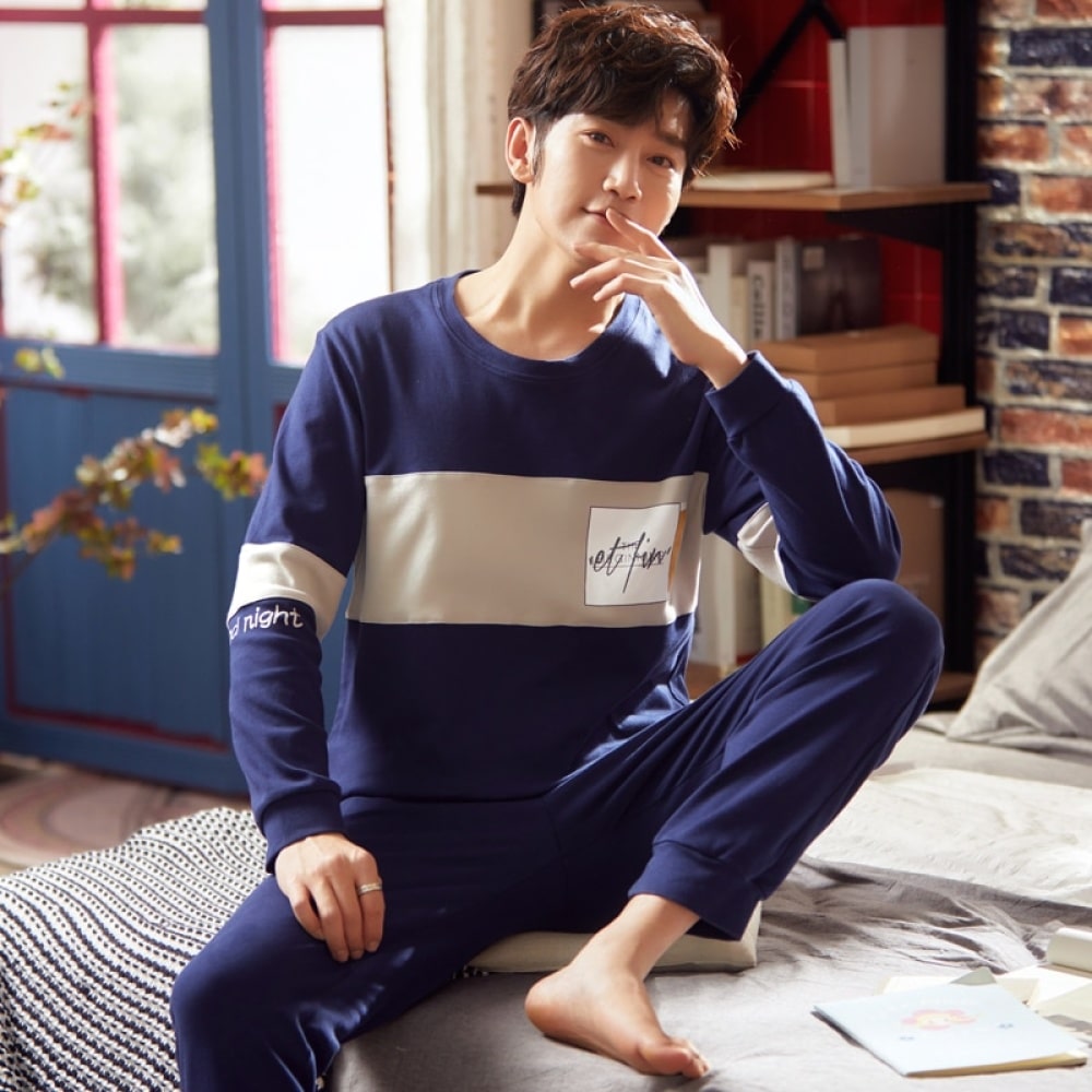 Pijama de algodón azul marino de dos piezas y manga larga que lleva un hombre sentado en la cama de una casa