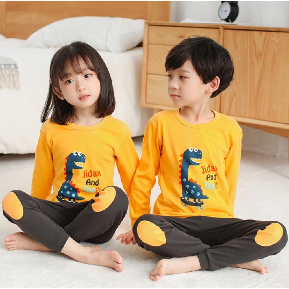 Pijama infantil con jersey amarillo de dinosaurio y pantalón marrón con dos niños vestidos con el pijama