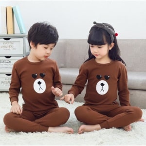 Pijama de primavera marrón con estampado de osos para niños con dos niños vistiendo el pijama y un sofá de fondo