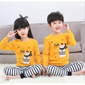 Pijama de primavera con jersey amarillo y pantalón blanco a rayas negras con dos niños vestidos con el pijama y un sofá de fondo