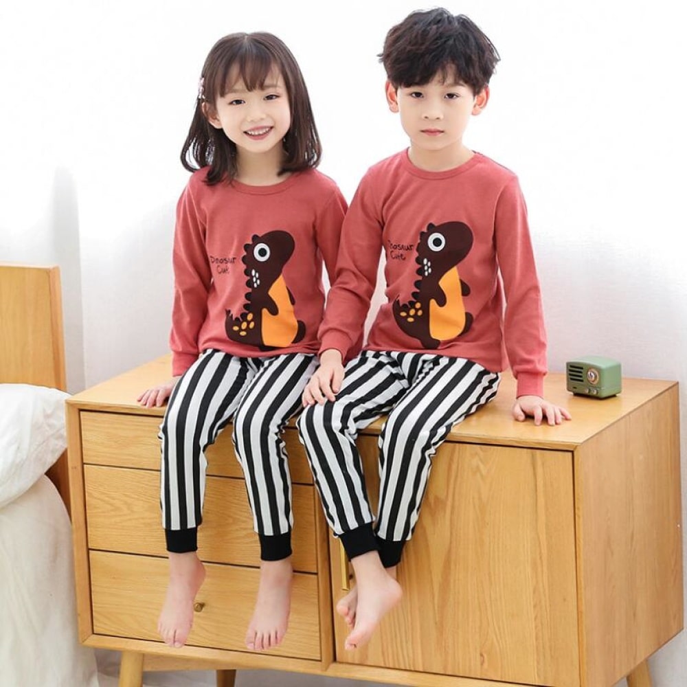 Pijama de primavera con jersey rosa y pantalón blanco a rayas negras para niños con dos niños vestidos con el pijama y de pie sobre el mueble