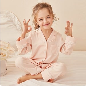 Pijama de dos piezas de encaje para "hacer como mamá" con una niña llevando el pijama con una cuna blanca y fondo rosa