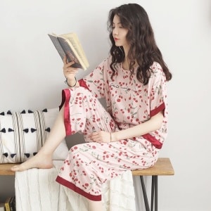 Pijama femenino de manga murciélago con estampado de flores rojas que lleva una mujer leyendo un libro sentada en una silla en una casa