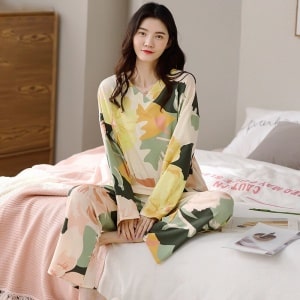 Pijama de mujer de manga larga y cuello en V con diseño floral que lleva una mujer sentada en la cama de una casa