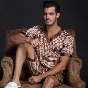 Pijama a cuadros de manga corta de satén de seda marrón para hombre con un hombre con el pijama puesto en el sofá