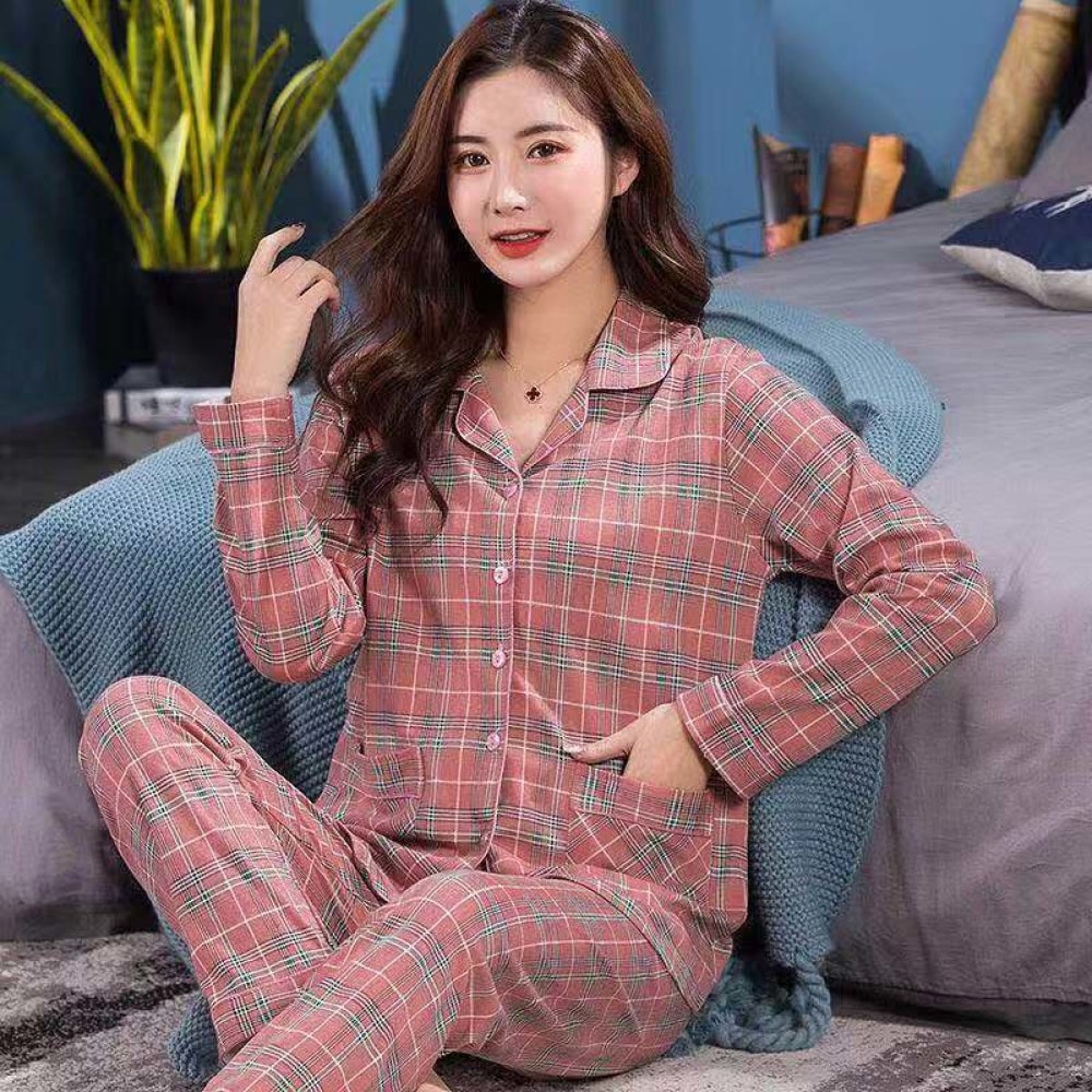 Pijama de mujer de dos piezas a cuadros con cuello doblado que lleva una mujer sentada en una alfombra delante de una cama en una casa