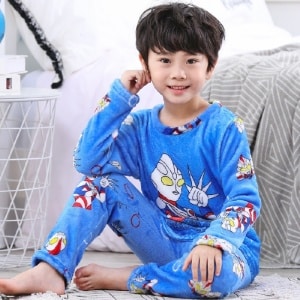 Pijama de franela azul de superhéroe para niño llevado por un niño sentado en una alfombra delante de una cama en una casa