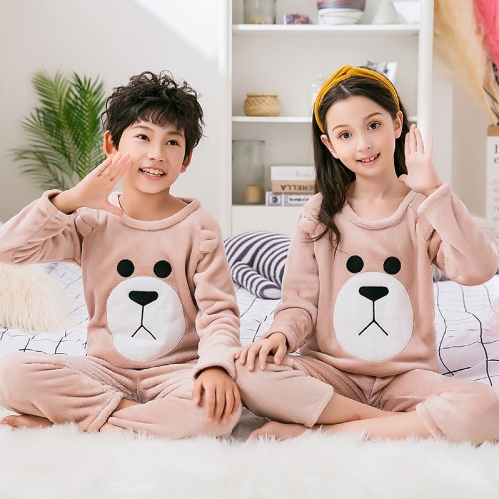 Pijama de vellón marrón para niños que llevan una niña y un niño sentados en la alfombra de una casa