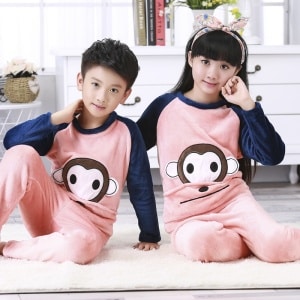 Pijama infantil de franela con estampado de monos que llevan un niño y una niña sentados en la alfombra de una casa