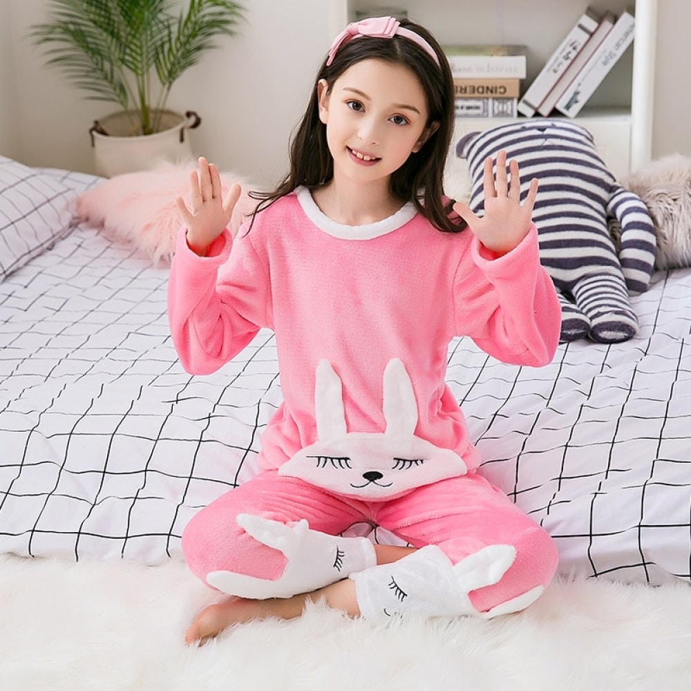 Pijama de franela rosa con estampado de conejitos para niña con diadema sentada en la cama de una casa