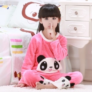 Pijama panda rosa de dos piezas para niña llevado por una niña sentada en una alfombra delante de una cama en una casa