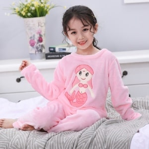 Pijama de franela de manga larga con estampado de sirenas para niña que lleva una niña en la cama de una casa