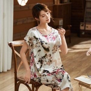Pijama blanco de satén de dos piezas con estampado de flores que lleva una mujer sentada en una silla en una casa