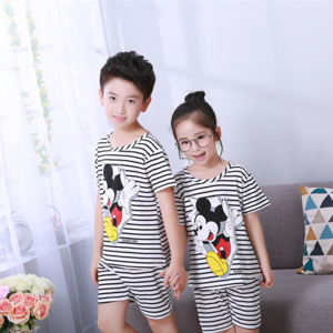 Pijama de verano a rayas blancas y negras con estampado de Mickey Mousse para niños que llevan un niño y una niña delante de una silla en una casa