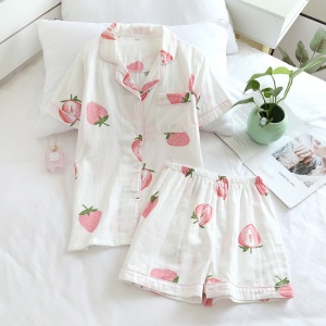 Pijama de verano de manga corta con estampado de fresas para mujer sobre una cama con un jarrón pequeño y una flor dentro en una casa