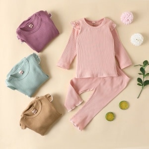 Pijama sencillo de algodón para niña con varios pijamas doblados y fondo beige