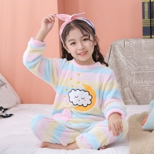 Pijama infantil de forro polar con los colores del arco iris que lleva una niña en la cama de una casa