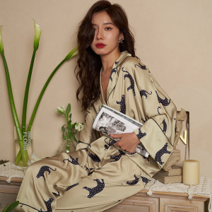 Pijama beige con estampado de leopardo que lleva una mujer sentada en un mueble sosteniendo una revista frente a una pared beige