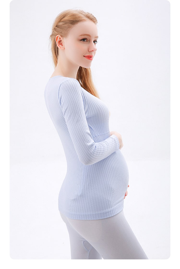 mujer embarazada tocándose el vientre con una mano, vestida con un pijama azul compuesto de pantalón y jersey de manga larga