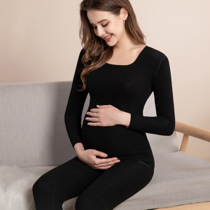 joven embarazada sentada en pijama negro, sonriendo mientras se toca su vientre redondo