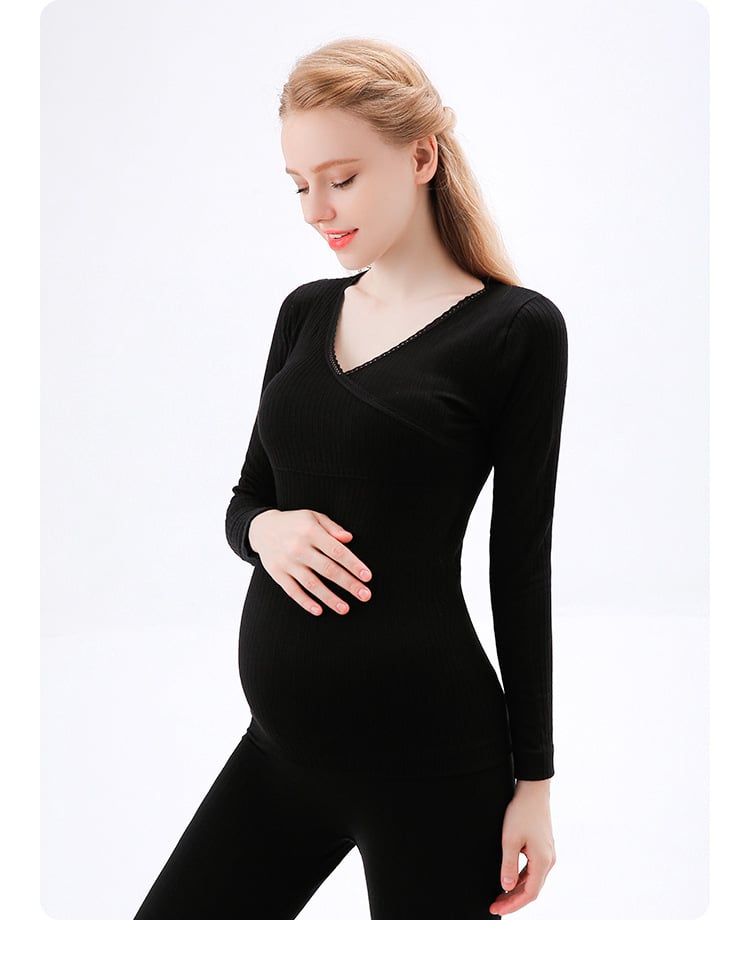 mujer embarazada tocándose el vientre con una mano, vestida con un pijama negro compuesto por un pantalón y un jersey de manga larga