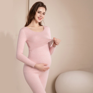 Mujer morena embarazada con pijama de maternidad rosa, se está tocando su vientre redondo con una mano y tirando de la parte superior del pijama con la otra