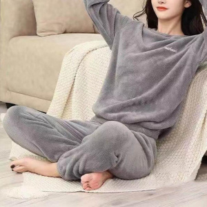 mujer joven vestida con un pijama de pilou gris, está sentada en un plaid junto a un sofá, en el suelo, con las manos cruzadas detrás de la cabeza