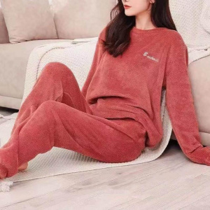 mujer joven con pijama rojo pilou pilou, está sentada en un plaid junto a un sofá en el suelo